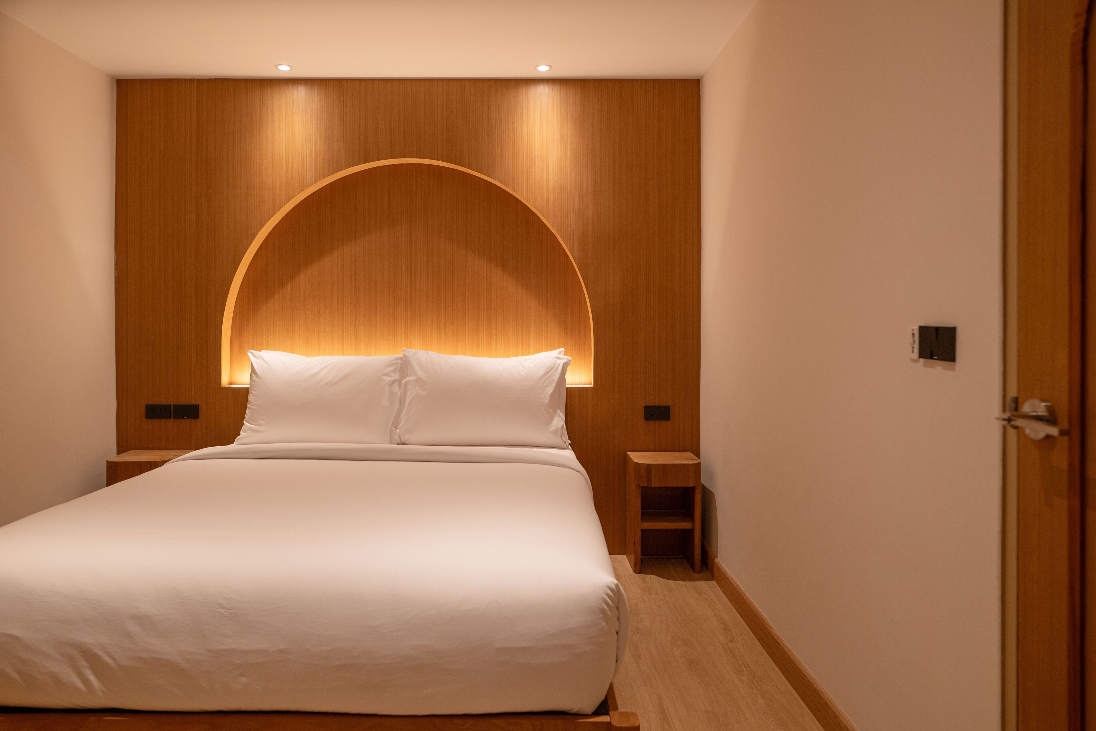 A hotel room with a large bed, wooden headboard, bedside tables, and a door.