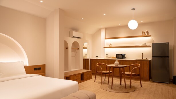 A modern hotel room with a bed, a small dining table with chairs, a kitchen area with a refrigerator, and a ceiling light. - Taupe Hotel (Chiang Mai)