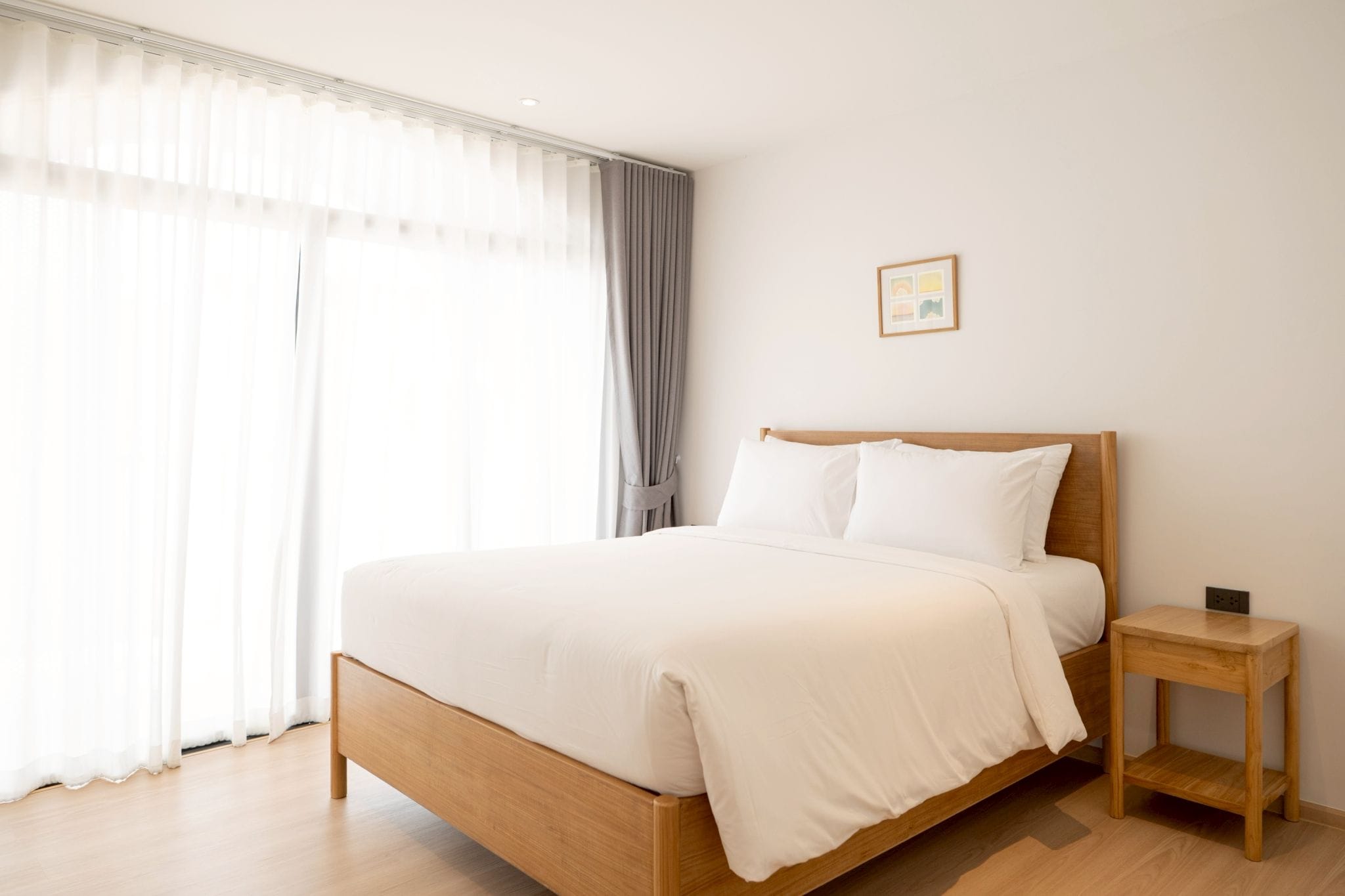 Une chambre à coucher avec un lit en bois, du linge de lit blanc, une table de chevet et une fenêtre avec des rideaux.