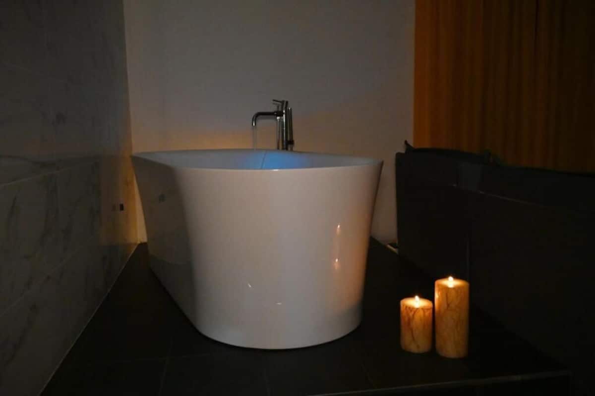 Een moderne badkamer met een groot wit wastafel, een kraan en twee brandende kaarsen op een donker aanrecht.