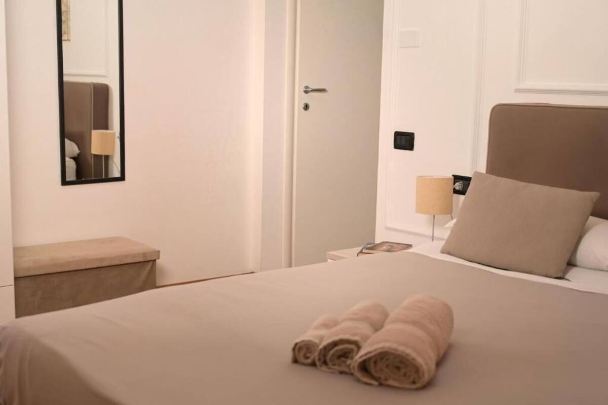 Een hotelkamer met een bed, nachtkastje, lamp en een deur.