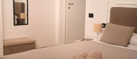A hotel room with a bed, a bedside table, a lamp, and a door.