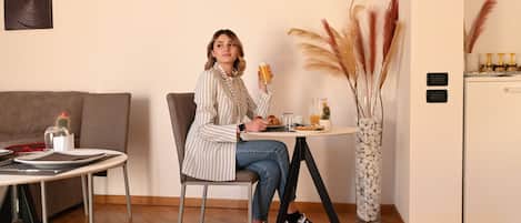 A person sitting at a table with a cup, a plate with food, and a vase with plants.