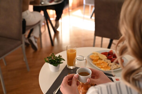 A person holding a cup of coffee at a table with a plate of food, a glass of juice, and a small plant. - Palace Eight Suites & Spa (Cosenza)