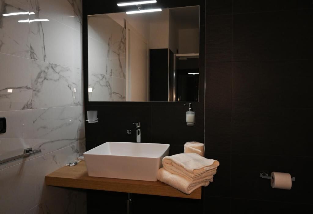 Un baño moderno con pared de azulejos de mármol, un lavamanos blanco y un espejo encima.