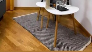 Una stanza piccola e moderna con un tavolo bianco, una sedia grigia, un vaso bianco con fiori e un oggetto nero sul tavolo.