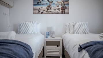 Habitación de hotel con dos camas, una mesita de noche con lámpara, botellas de agua y un cuadro en la pared.