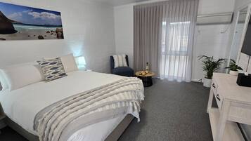 A hotel room with a bed, a desk, a chair, a TV, a window with curtains, and a wall-mounted picture.