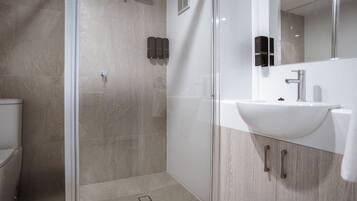 Un baño moderno con cabina de ducha de vidrio, un lavamanos blanco y un espejo.