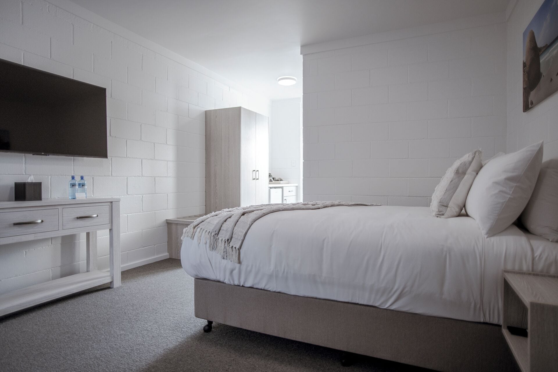 A bedroom with a bed, a TV, a desk, and a bathroom visible in the background.