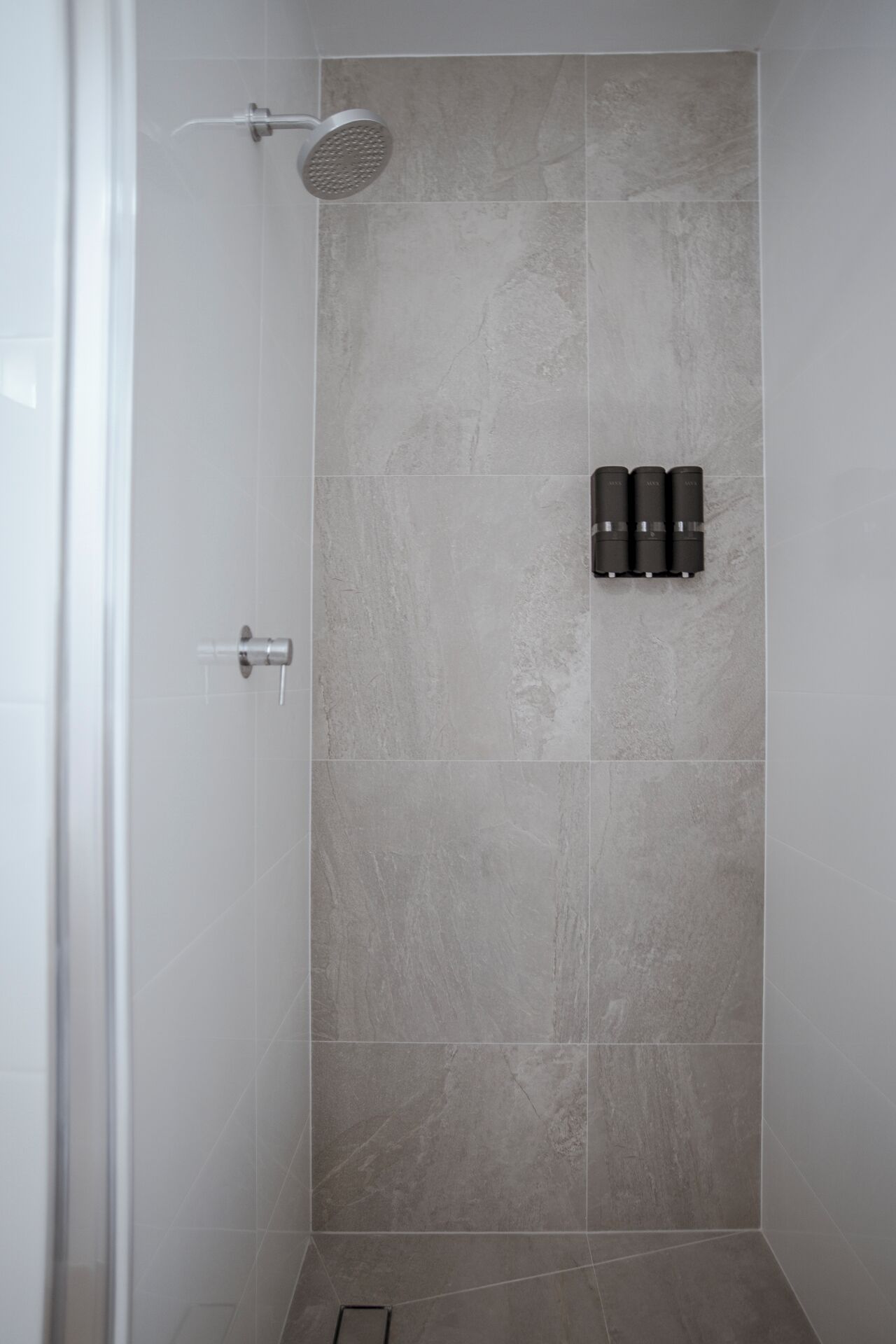 A shower with a handheld showerhead, a wall-mounted control panel, and a tiled floor.