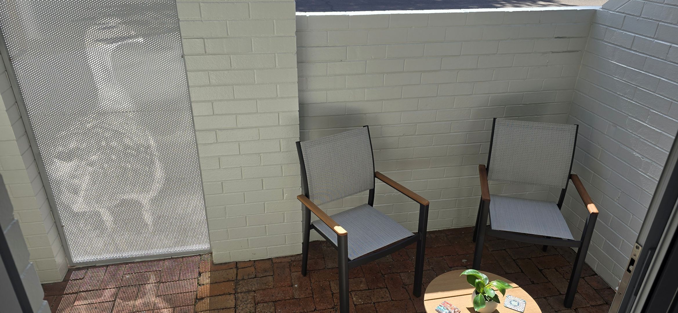 A small patio area with two chairs and a table, a white brick wall, and a metal gate.