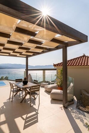A terrace with a table and chairs, a potted plant, and a view of the sea. - Studios Limnionas (Limnionas)