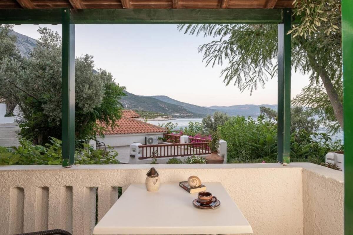 A balcony with a table set for two, overlooking a scenic view of a coastal area with mountains and a body of water.