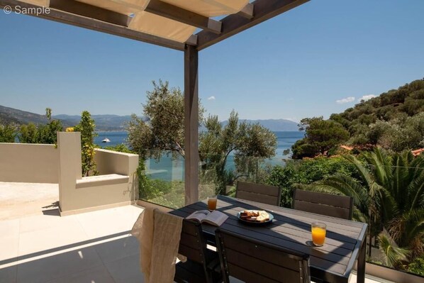 A terrace with a table, chairs, and a view of a lake and mountains.