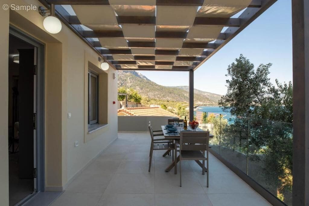 A balcony with a table and chairs, a pergola overhead, and a view of a mountainous landscape.