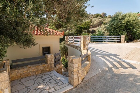 A stone-walled entrance with a bench, a small building with a tiled roof, and a gate. - Studios Limnionas (Limnionas)