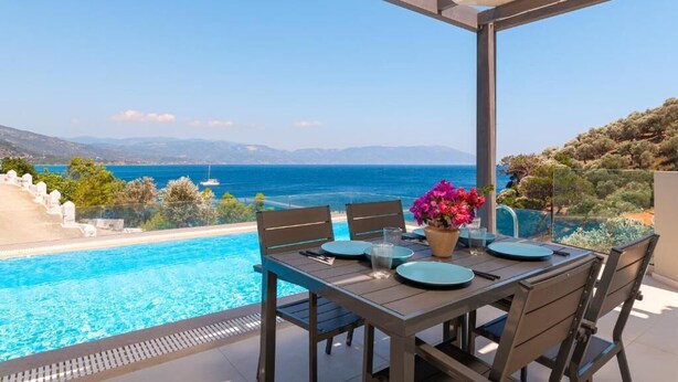 Une terrasse avec une table dressée pour deux personnes, donnant sur une piscine et la mer.
