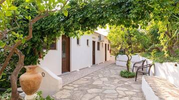 A stone-paved courtyard with white walls, a wooden door, and a bench.