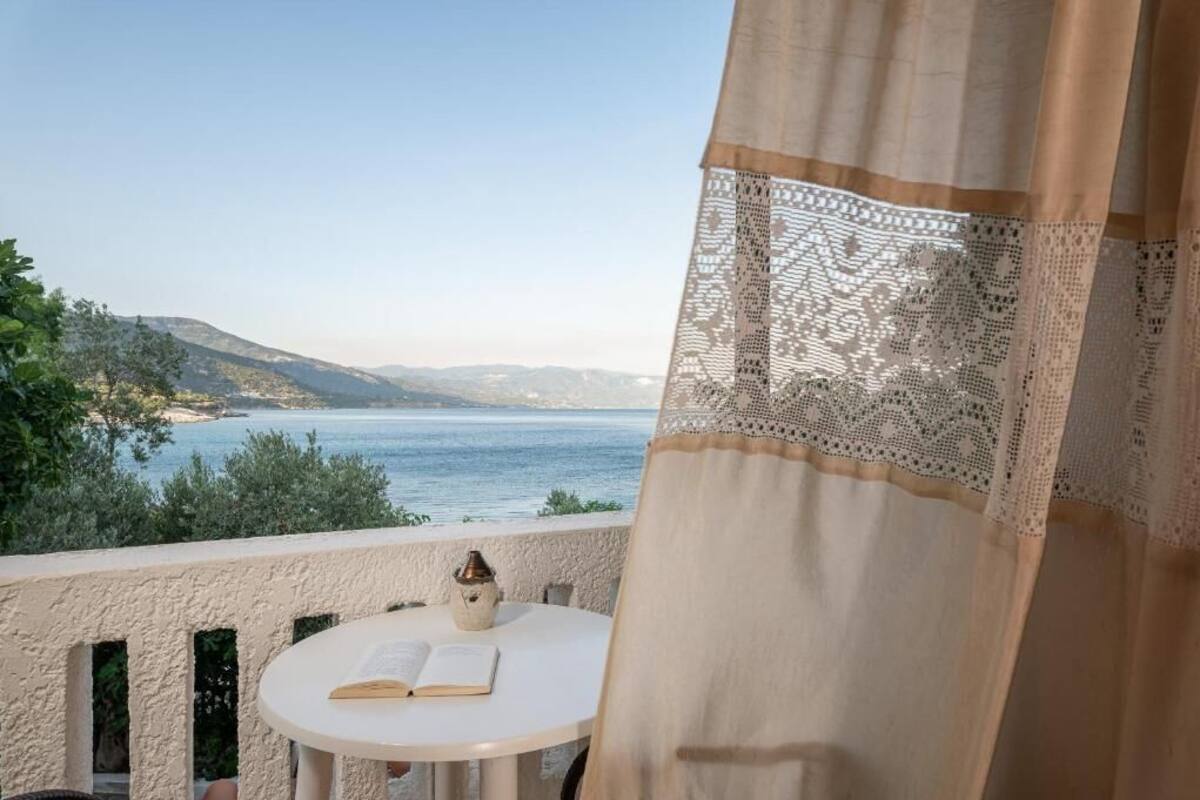 A balcony with a view of the sea, a table with a book and a vase, and a lace curtain.