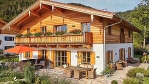 Eine Holzhütte mit Balkon, Sitzgelegenheit im Freien und einem Garten.