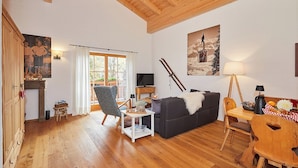 Ein gemütliches Wohnzimmer mit Holzboden, einer Couch, einem Sessel, einem Fernseher und einem Bild von einem Skifahrer.
