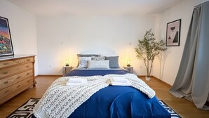 Ein Schlafzimmer mit Bett, Nachttischen, einem Schminktisch, einer Zimmerpflanze und Bildern an der Wand.