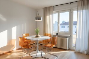 Une pièce moderne avec une table ronde, quatre chaises orange, une plante en pot, un lampadaire et une grande fenêtre avec des rideaux.
