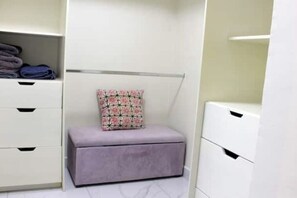 A neatly organized closet with a padded bench, a hanging organizer, and a folded towel on the shelf. - Modern furnished house in the heart of GDL (Guadalajara)