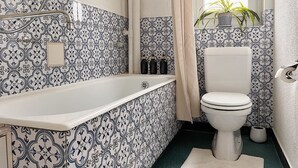 Un baño con una bañera blanca, un inodoro blanco y baldosas estampadas.