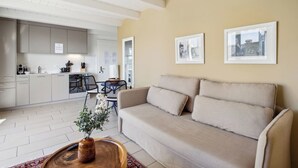 A modern living room with a beige sofa, a wooden coffee table with a vase, and a dining area with a black chair and table. - Comfortable Flat with Terrace in Zurich (401-16) (Zürich)
