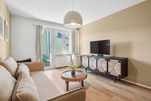Una sala de estar con un sofá, una mesa de centro, un televisor sobre un mueble y vistas a través de una puerta de vidrio.