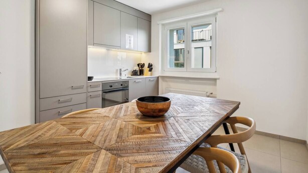 Eine moderne Küche mit grauen Schränken, einem Holzesstisch und einem Fenster mit weißen Fensterläden.