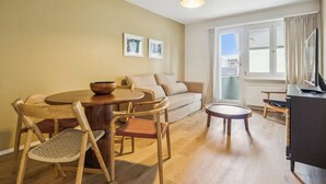 Un salon avec une table ronde en bois, deux fauteuils en osier, un canapé et un meuble pour la télévision.