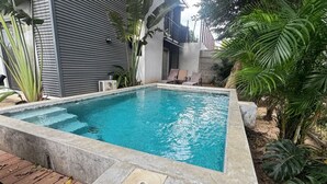 A rectangular swimming pool with a concrete edge, surrounded by tropical plants and a wooden deck. - Nangu Apartment in Coco (Coco)