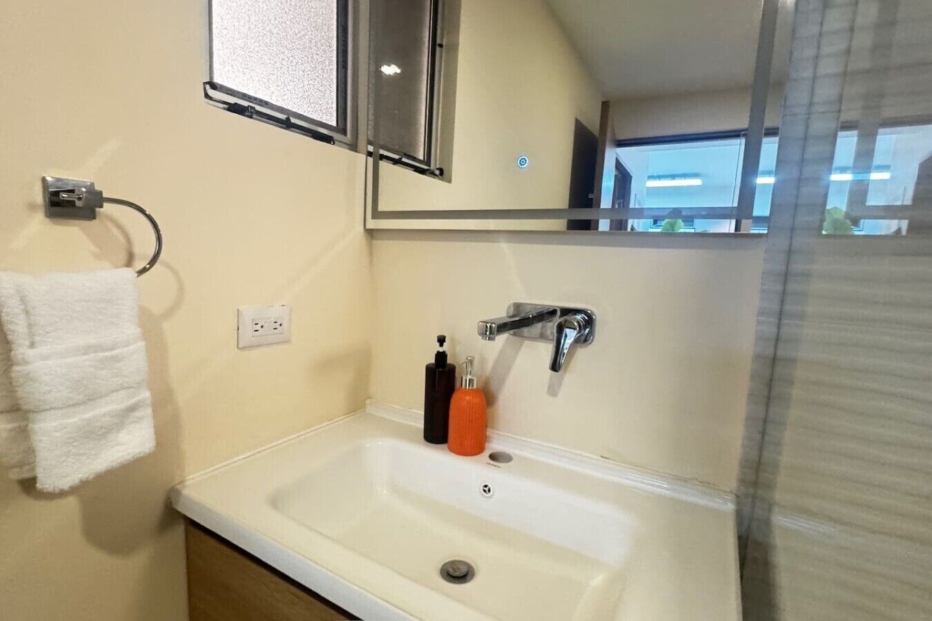 Een badkamer met een witte wastafel, een spiegel, een handdoekhouder en een zeepfles.