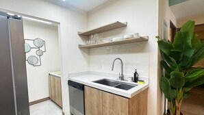 A compact kitchen with a dishwasher, a sink, and a countertop. There are wooden cabinets and a potted plant. - Nangu Apartment in Coco (Coco)