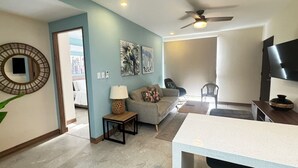 A living room with a sofa, a coffee table, a TV, and artwork on the wall. - Nangu Apartment in Coco (Coco)