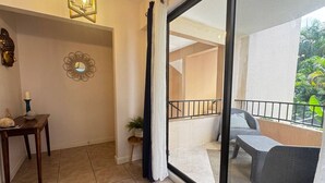 Un balcon donnant sur un espace verdoyant, un coin repas avec une table et des chaises, et un miroir décoratif accroché au mur.