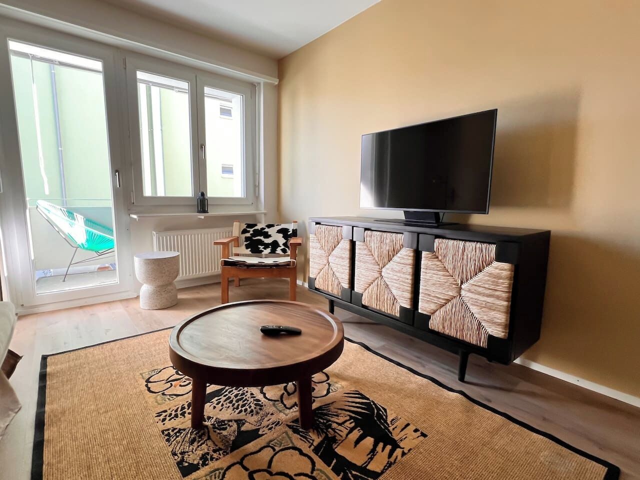 Una sala de estar con un televisor sobre un mueble, una silla y una mesa redonda.