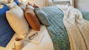 A neatly arranged bedroom with a bed, pillows, a blanket, a cup of tea, and a book. - Elegant City Apartment with Balcony! (101-16) (Zürich)