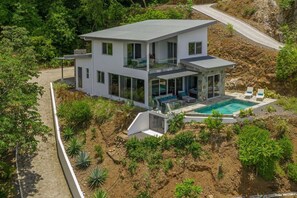 A modern two-story house with a swimming pool, surrounded by greenery and a paved driveway. - Modern & Scenic Haven | Breathtaking Views - Pool (Coco)