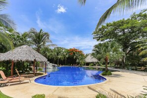 A swimming pool with lounge chairs, palm trees, and thatched umbrellas. - Modern & Scenic Haven | Breathtaking Views - Pool (Coco)