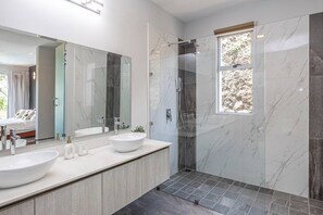 A modern bathroom with a large mirror, two sinks, a shower, and a window. - Modern & Scenic Haven | Breathtaking Views - Pool (Coco)