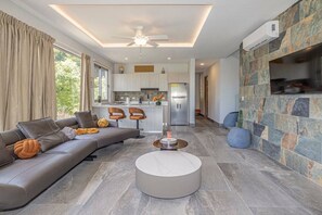 A modern living room with a sectional sofa, a round coffee table, and a stone accent wall. - Modern & Scenic Haven | Breathtaking Views - Pool (Coco)