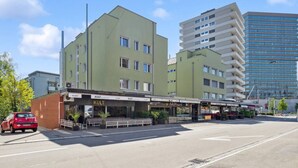 Een gebouw met een groene gevel, een bar genaamd 'KULT' op de begane grond, en een modern hoogbouw op de achtergrond.
