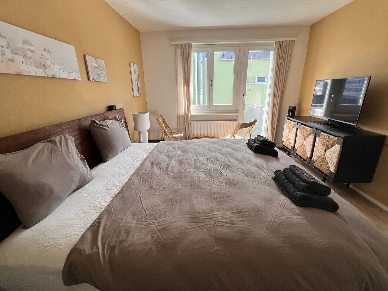 A hotel room with a large bed, a television, and a view of the outside.