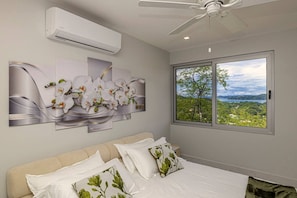 A bedroom with a bed, a ceiling fan, an air conditioning unit, and a window with a view of greenery. - Luxury Ocean View Villa with Infinity Pool (Coco)