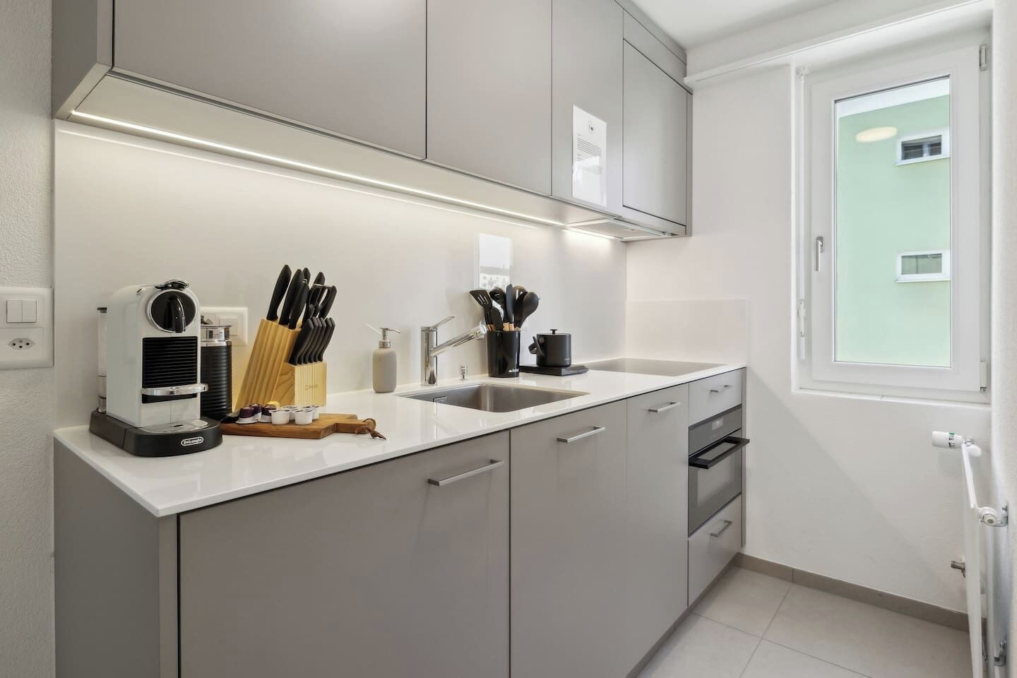 A modern kitchen with a built-in coffee machine, knife block, and utensils on the counter.