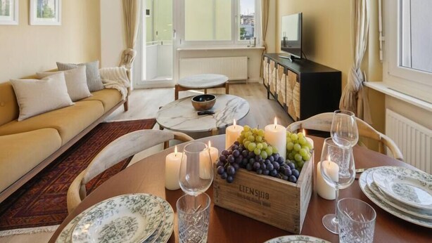 Una sala de estar acogedora con un sofá, una mesa de comedor dispuesta con platos y velas, y un televisor al fondo.